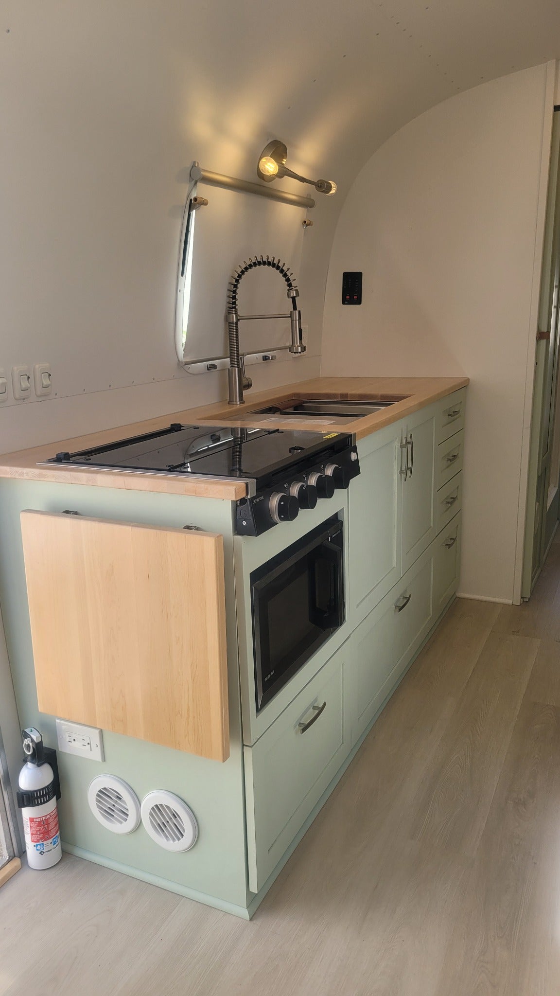 Custom NuAbode Airstream galley with sage cabinetry, integrated appliances and handcrafted wood worktop