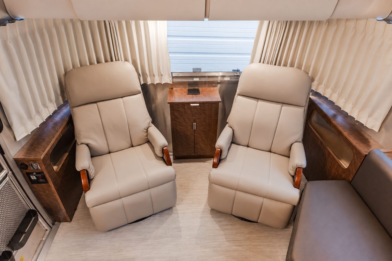 Two cream recliners installed by NuAbode in an Airstream, with wood side cabinetry and a center cabinet